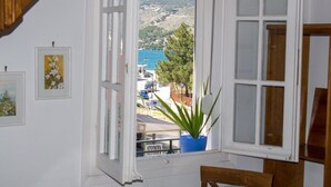A room with a large window overlooking a coastal area, a potted plant, and framed artwork on the wall.