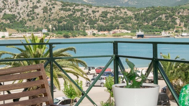 A balcony with a view of a coastal area, including a body of water, vehicles, and buildings in the background.
