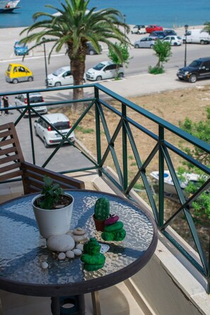 Een balkon met een tafel, planten in potten en uitzicht op de straat en zee.