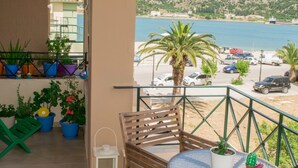 A balcony with a view of a beach and parked cars, featuring potted plants and a wooden chair.