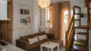 A cozy living room with a brown sofa, a white coffee table, a large window with sheer curtains, a wooden ladder, and a bookshelf filled with books.