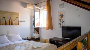 A hotel room with a bed, a TV, a window with curtains, and artwork on the walls.