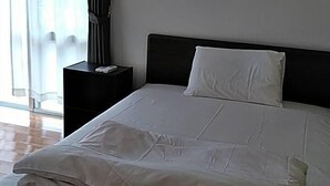 Un lit bien fait, avec du linge de lit blanc, une tête de lit sombre et un climatiseur fixé au mur.
