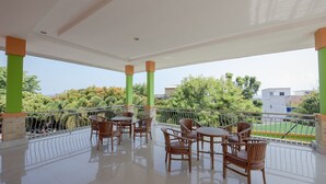 A covered outdoor area with a tiled floor, green pillars, and wooden furniture. - OYO 1164 Edotel Mahligai By Smkn 2 Tanjung Pinang (Tanjung Pinang)
