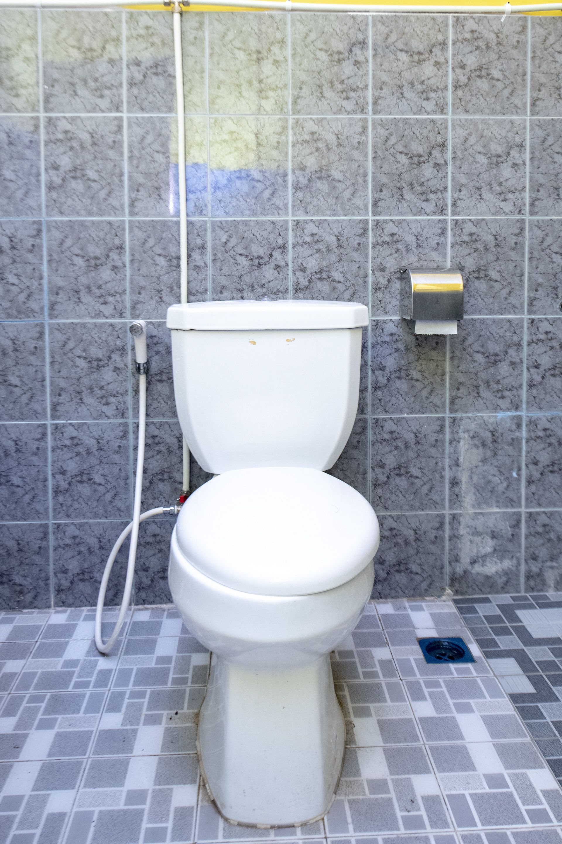 A bathroom with a toilet, a paper towel dispenser, and a floor drain.