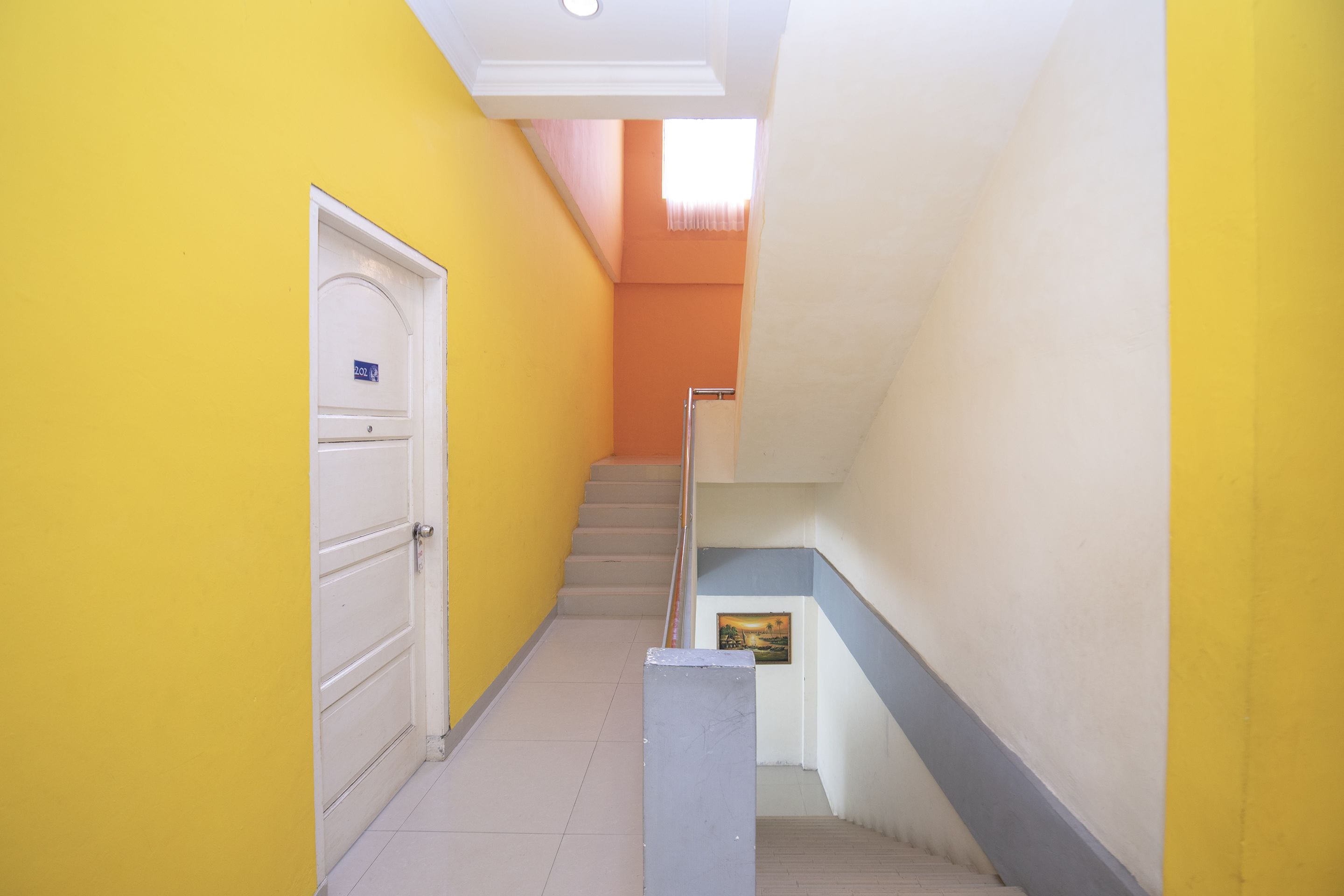 Un pasillo estrecho con paredes amarillas, una puerta blanca y una escalera con barandilla azul.