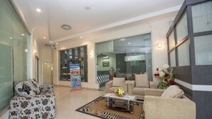 A spacious lobby with a sofa, armchair, and a coffee table with flowers. There is a glass wall and a large window. - OYO 1164 Edotel Mahligai By Smkn 2 Tanjung Pinang (Tanjung Pinang)