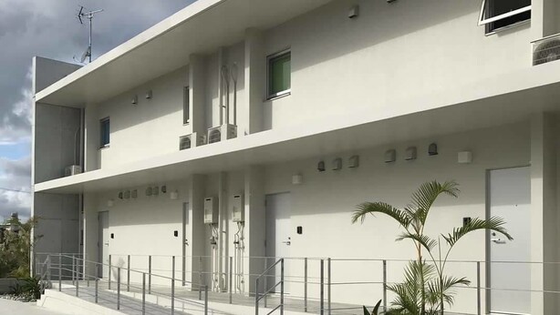 A modern building with a flat facade, multiple windows, and a gated entrance. - Guest House Minami II (Nanjo)