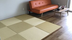 A room with a tatami mat floor, a wooden coffee table, an orange sofa, and a small table with a remote control. - Guest House Minami II (Nanjo)