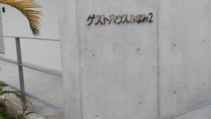 A concrete wall with a plaque that reads "Guest House" in Japanese. - Guest House Minami II (Nanjo)