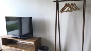 A room with a wooden TV stand, a black trash bin, and a wooden clothes rack with hangers. - Guest House Minami II (Nanjo)