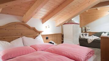 A bedroom with a wooden ceiling, a bed with pink bedding, a wardrobe, and a sofa with cushions.