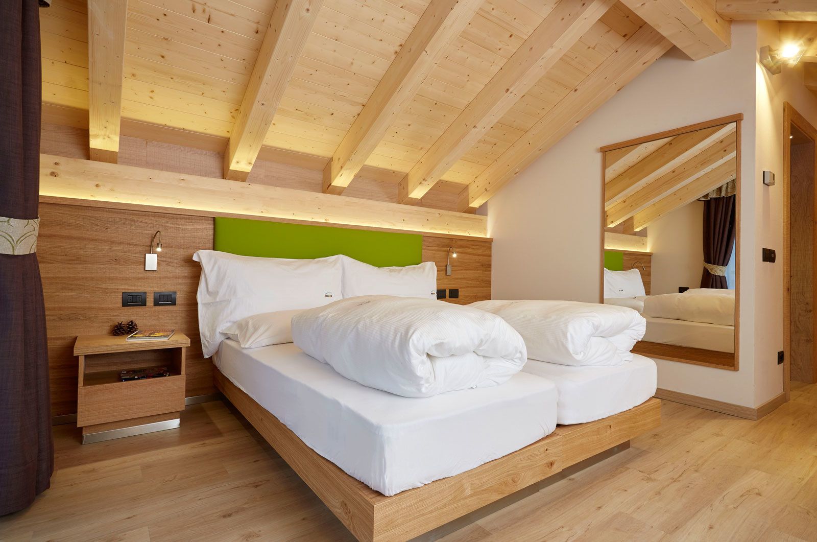 A modern bedroom with a wooden ceiling, a large bed with white bedding, a nightstand, and a mirror.