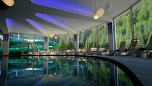 Une piscine intérieure moderne avec des parois en verre transparent, des chaises longues et une vue sur une forêt par les fenêtres.