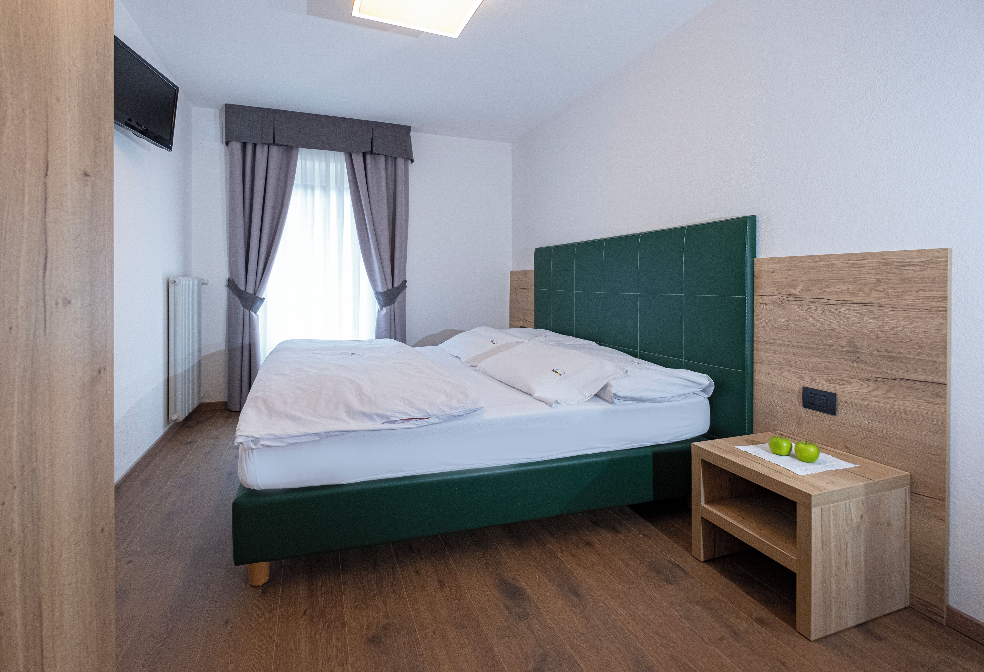 A neatly made bed with white linens, a green headboard, and a wooden nightstand with two apples.