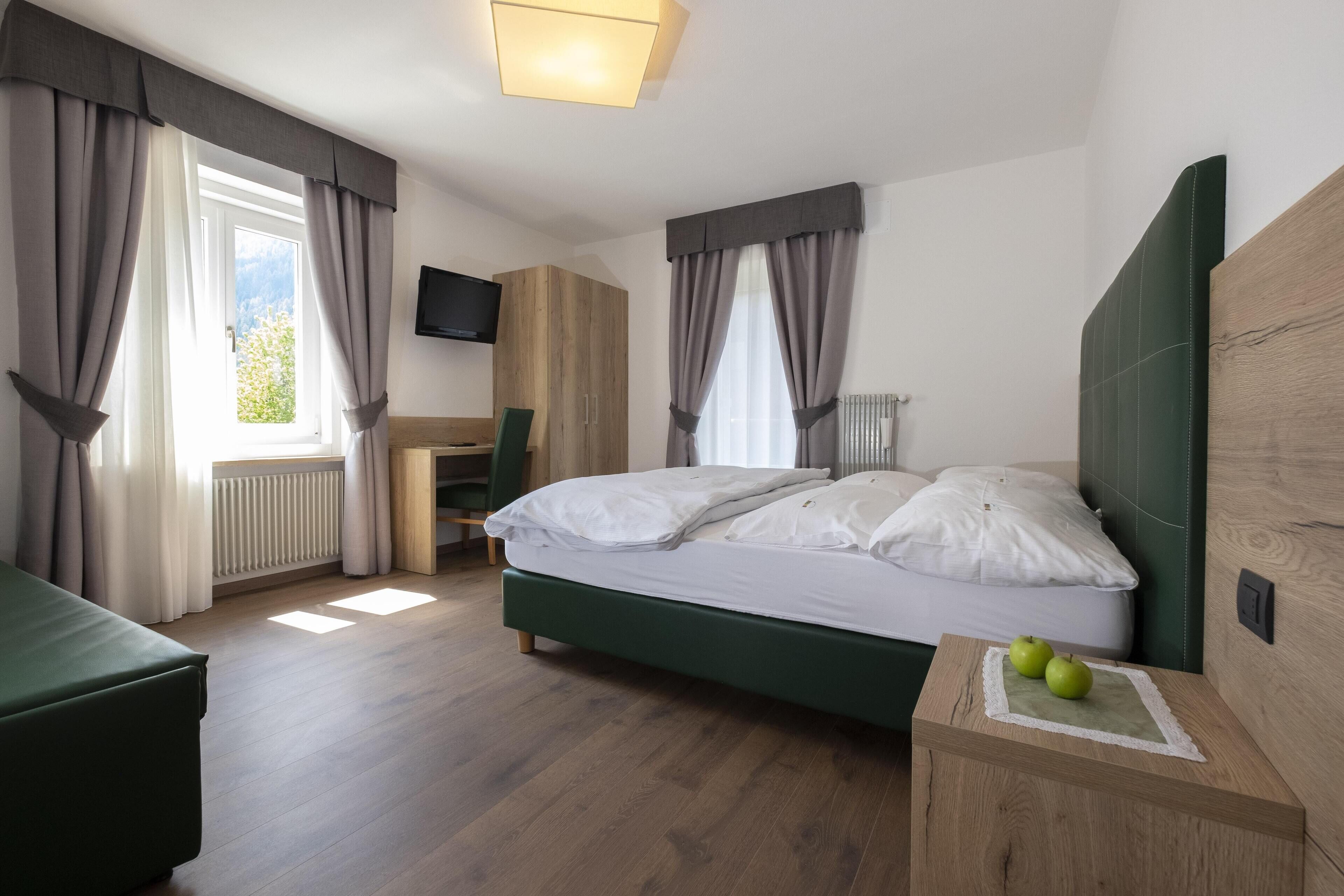 A bedroom with a bed, a desk, a chair, and a TV.