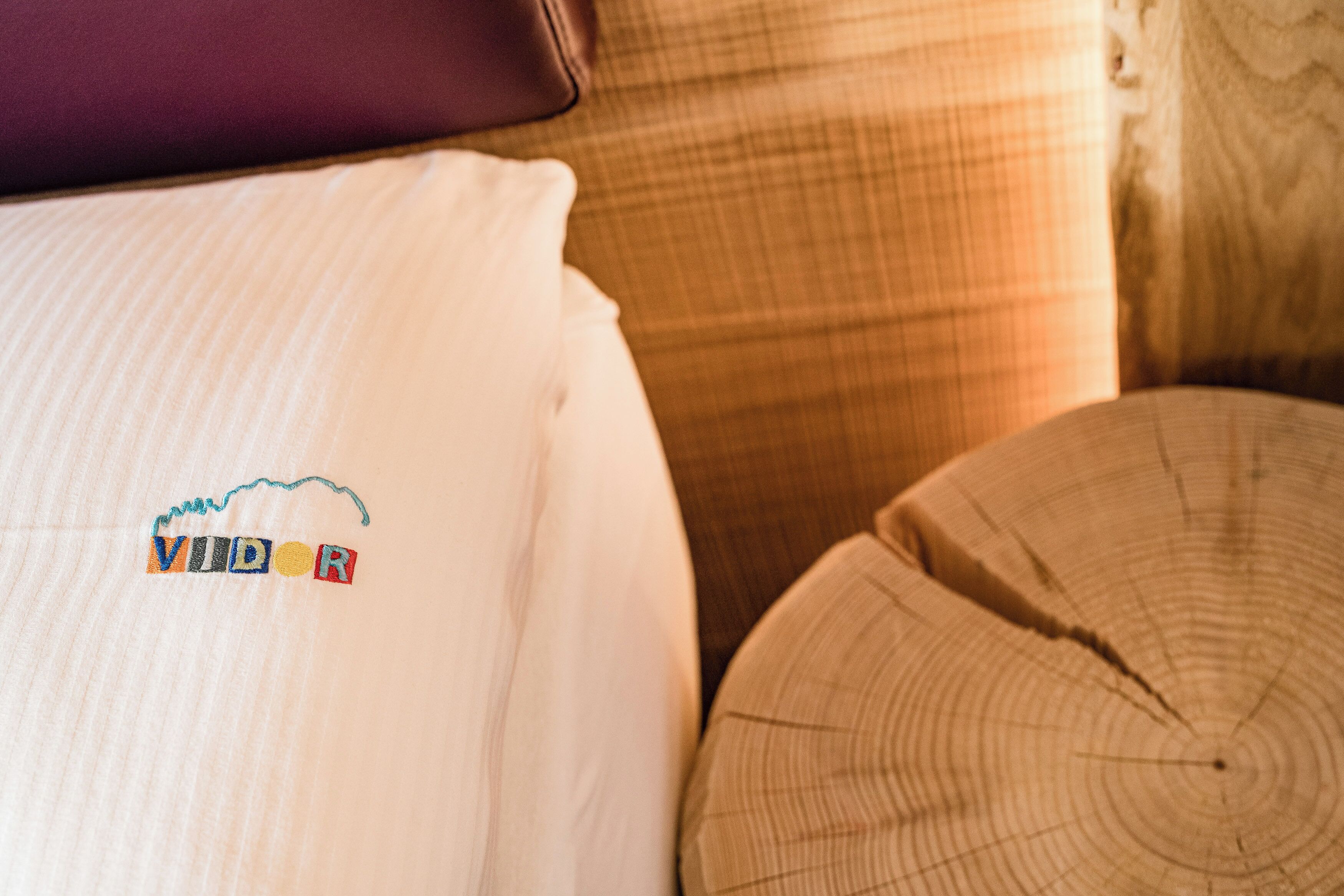 A bed with a pillow featuring embroidered text, a wooden headboard, and a round wooden stool.