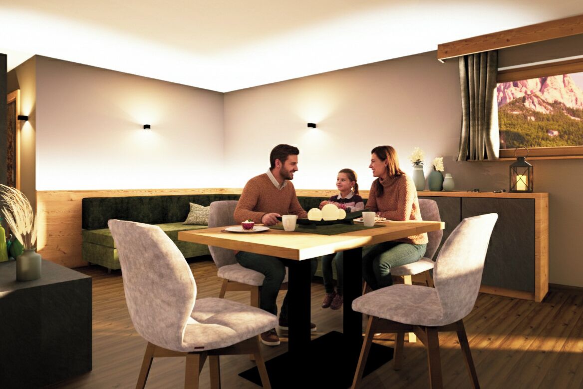 Ein moderner Essraum mit einem Holztisch, vier Stühlen, einer Couch und Blick auf Berge durch ein Fenster.