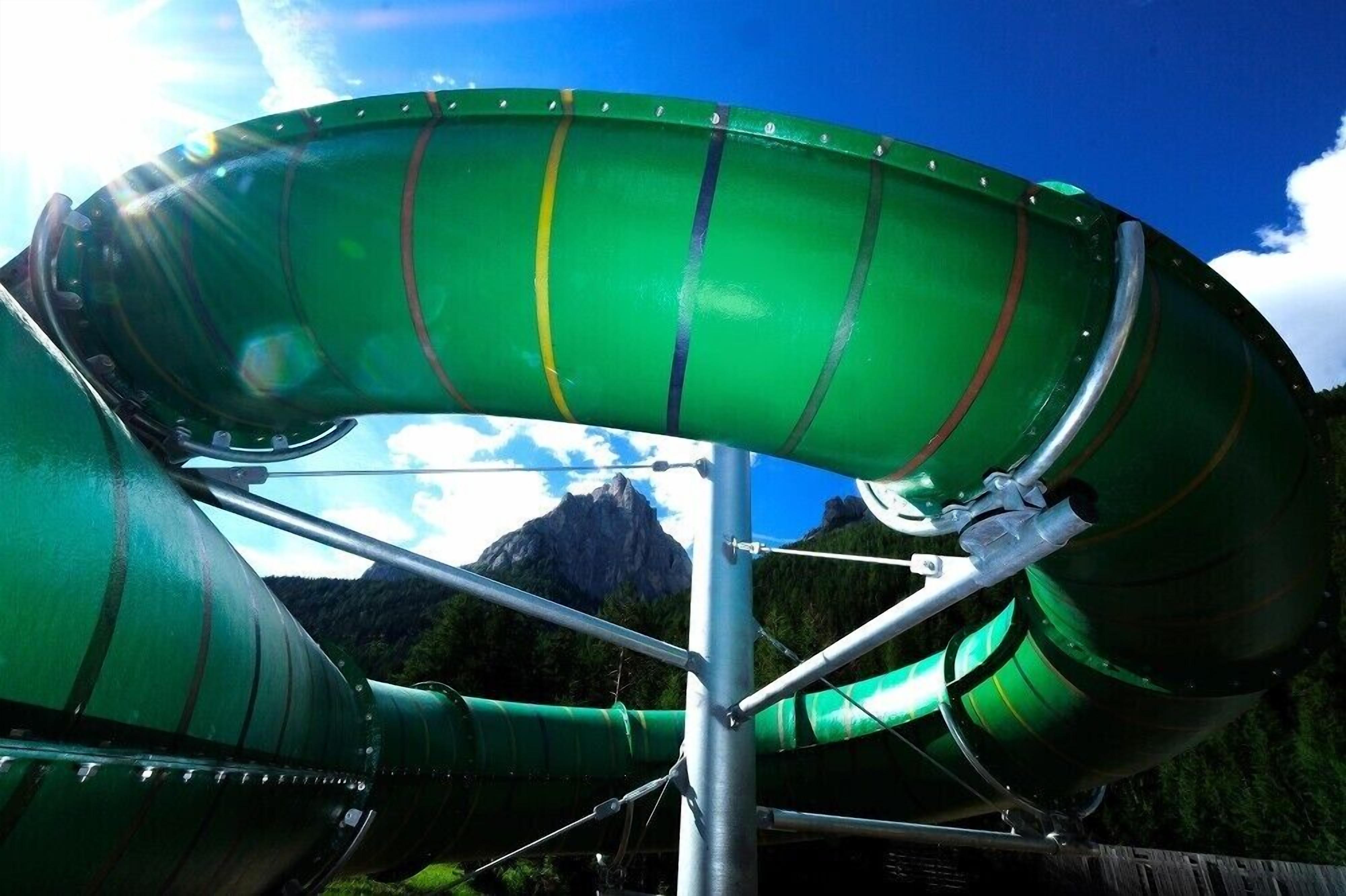 Una gran estructura de tobogán acuático, de color verde, con una estructura de soporte metálico, frente a un telón de fondo montañoso.