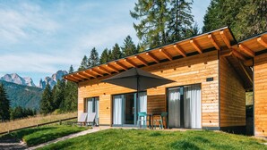 Une cabane en bois dotée d’une terrasse, de grandes fenêtres et offrant une vue sur la montagne.