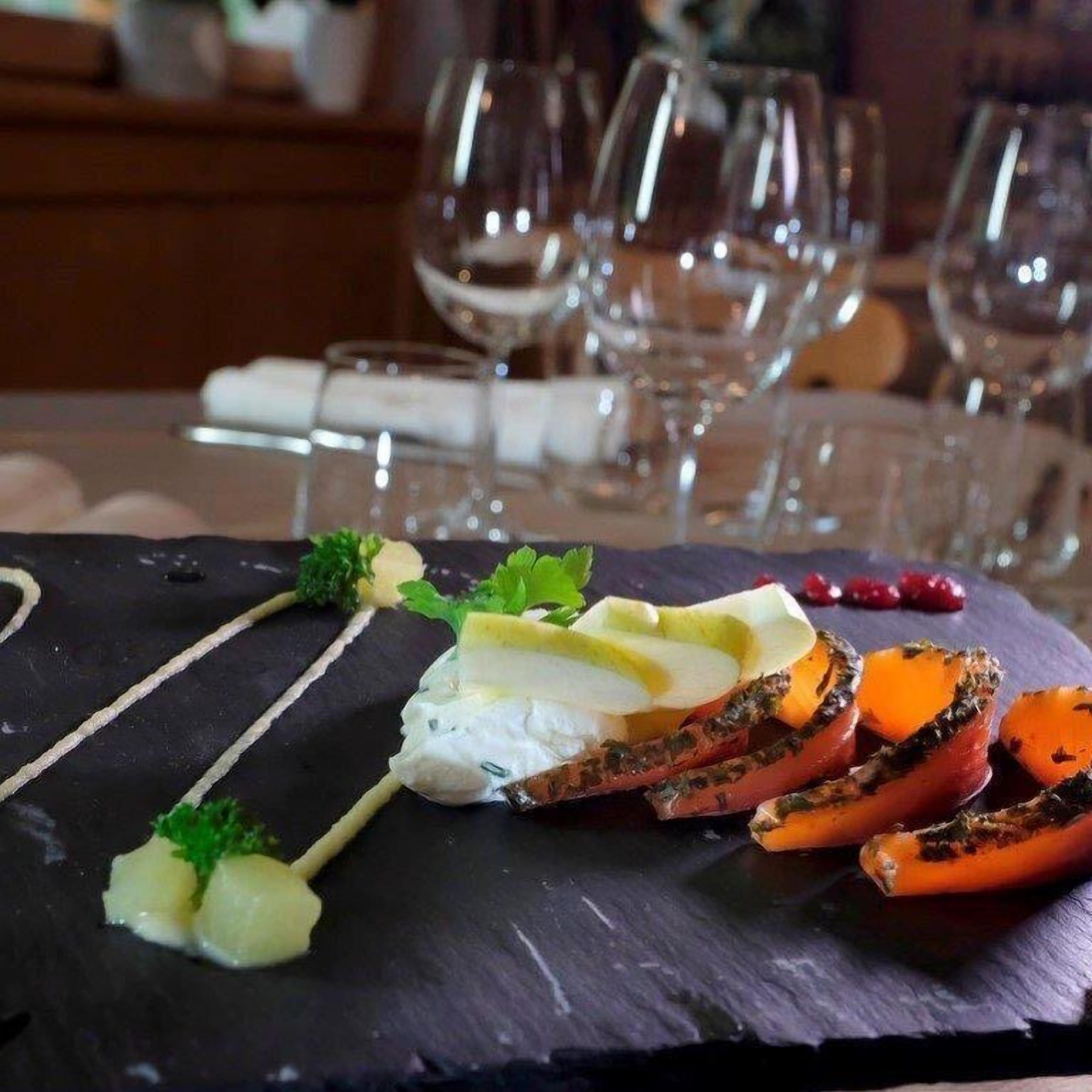 A dining table with a black slate serving board, a white creamy sauce, and roasted vegetables.
