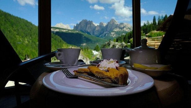 Une table avec une assiette de nourriture, une tasse et une théière, le tout placé devant un paysage de montagne.