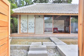 A traditional Japanese-style building with a tiled roof, sliding glass doors, and a small outdoor area with steps leading to a stone platform. - Kawasemi no su (Nago)