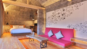 Una habitación moderna con techo de madera, una cama con ropa de cama blanca, un sofá rosa con cojines y una mesa de centro de madera.