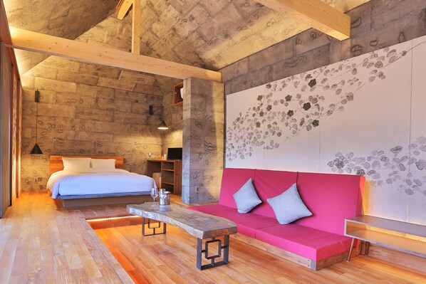 A modern room with a wooden ceiling, a bed with white linens, a pink sofa with cushions, and a wooden coffee table. - Kawasemi no su (Nago)