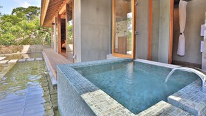 Un área de piscina moderna al aire libre, con una piscina azul cristalina, terraza de madera y puertas de cristal que dan a una zona cubierta.