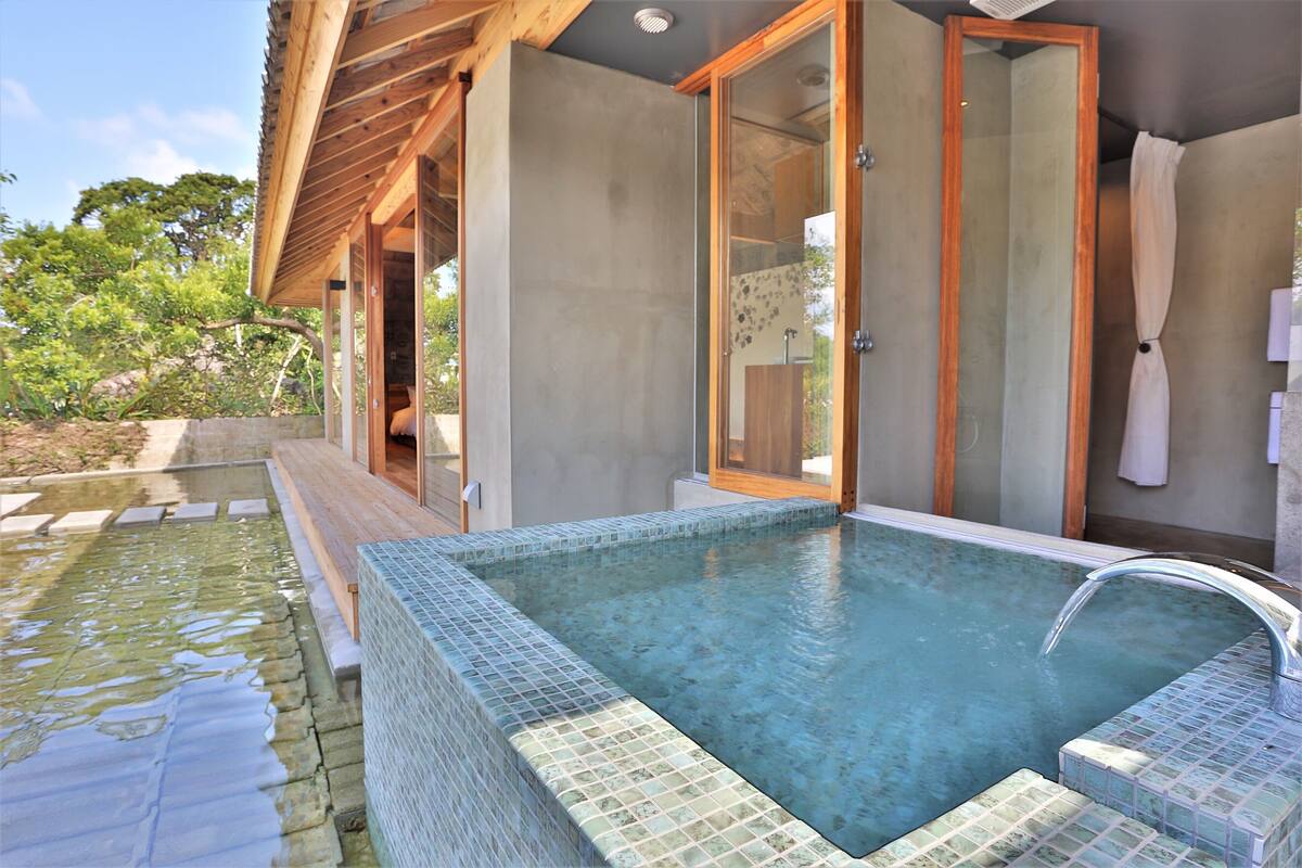A modern outdoor pool area with a clear blue pool, wooden deck, and glass doors leading to a covered area.
