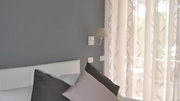 Une chambre à coucher avec un lit, deux oreillers, une table de chevet, une lampe et des rideaux légers.