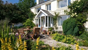 Ein Haus mit Garten, einer Veranda und verschiedenen Pflanzen und Blumen.