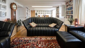 Ein Wohnzimmer mit einem schwarzen Ledersofa, einem gemusterten Teppich und einem Bücherregal voller Bücher.