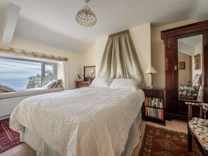 Un dormitorio con una cama grande, una ventana con vistas, una estantería y un espejo.