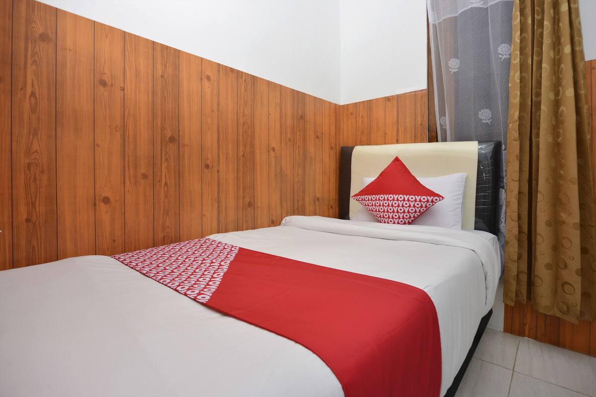 A hotel room with a wooden paneled wall, a bed with white and red bedding, and a curtain with a floral pattern.