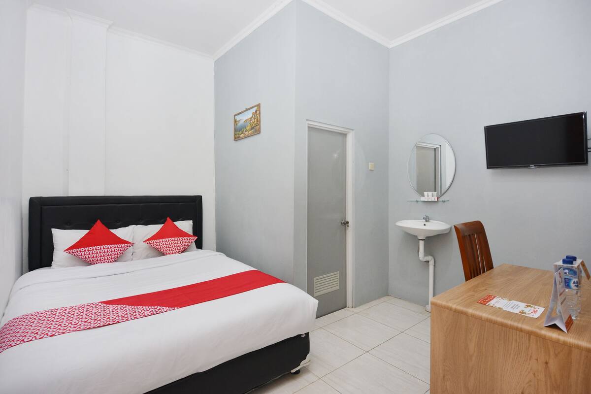 A hotel room with a bed, a wooden table, a TV, a mirror, and a sink.