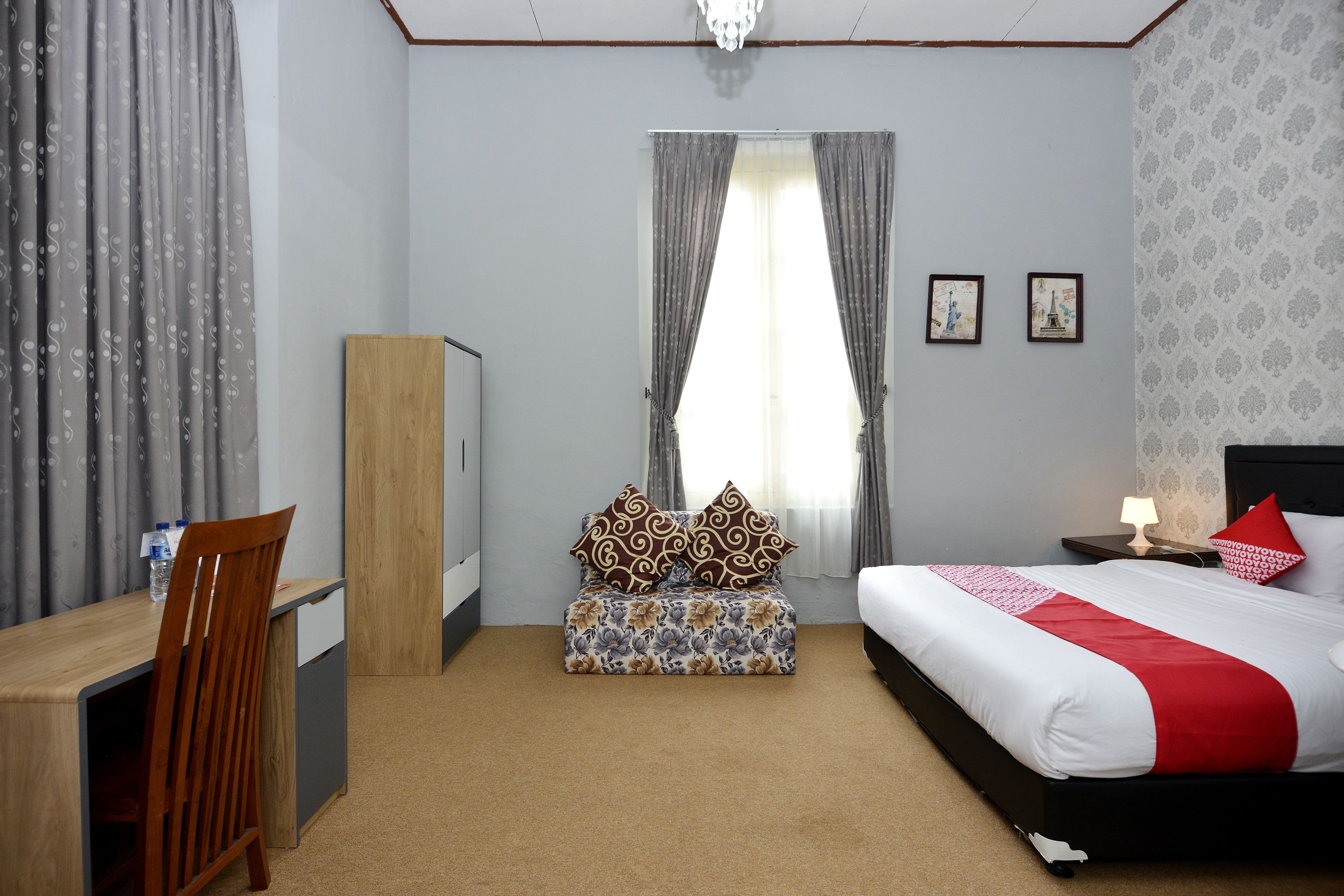 A hotel room with a bed, a desk, a chair, a small table, and a window with curtains.