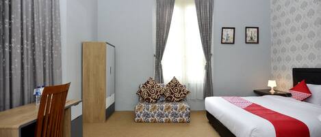 A hotel room with a bed, a desk, a chair, a small table, and a window with curtains.