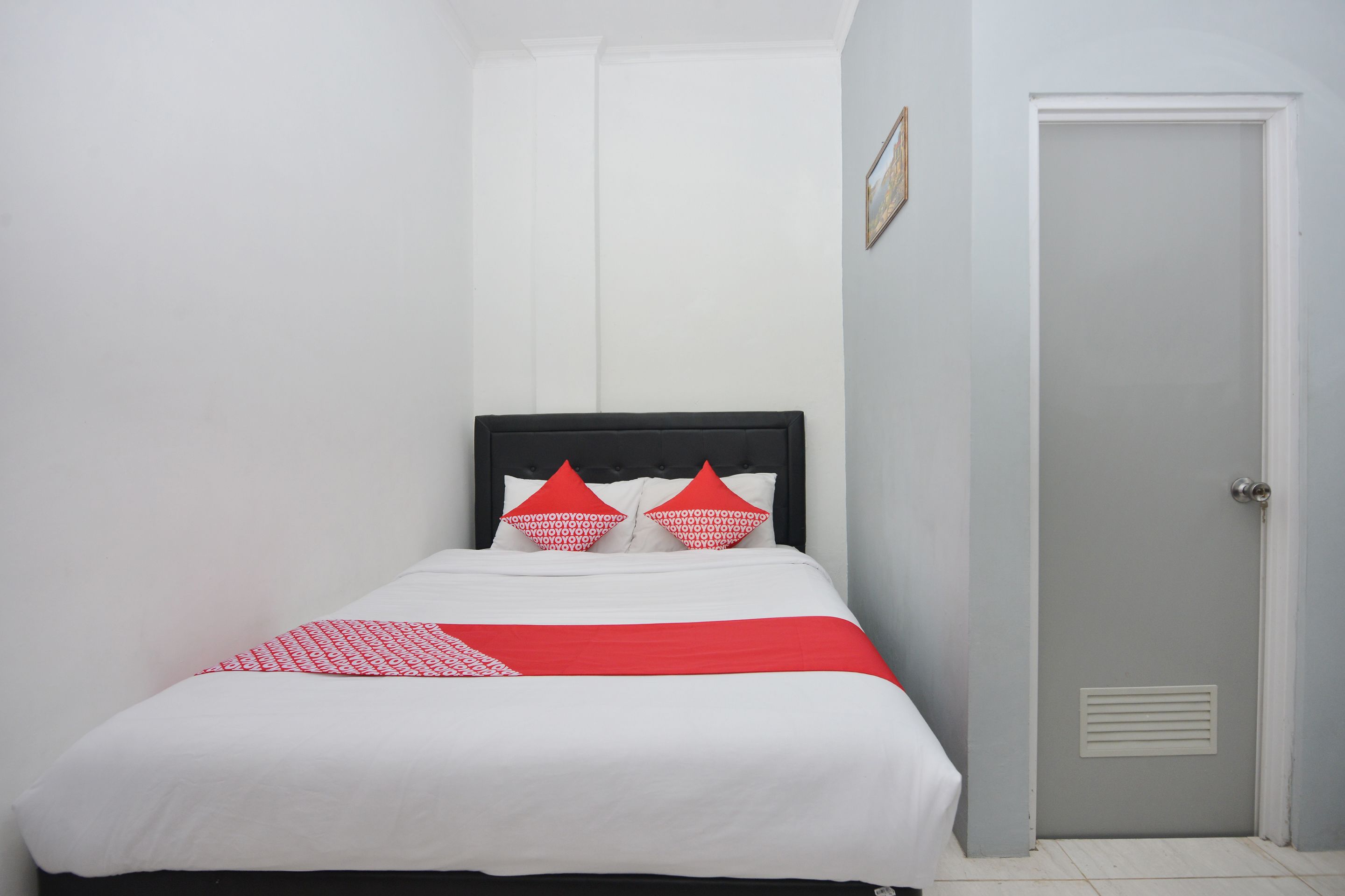 Un lit bien fait, avec une tête de lit noire, du linge de lit blanc et des touches de couleur rouge.