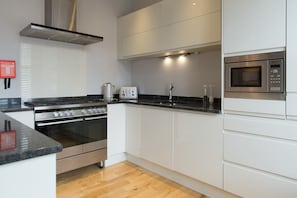 A modern kitchen with white cabinets, a stainless steel range, a built-in microwave, and a toaster. - Belford (Harrogate)