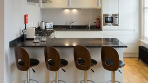 Une cuisine moderne dotée d’un îlot central, de tabourets de bar, de meubles blancs, d’un four à micro-ondes et d’une machine à café.