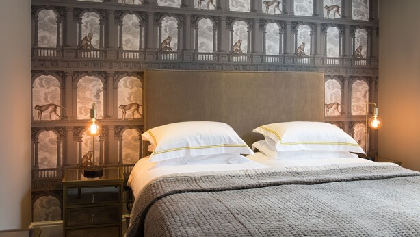 Une chambre avec un grand lit, deux tables de chevet, un mur orné d’une fresque représentant des singes et un luminaire moderne.