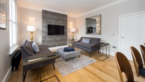 Un salon moderne doté d’un téléviseur à écran plat, de deux canapés, d’une table basse et d’un coin repas avec des chaises en bois.