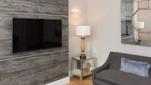 Un salon moderne avec un téléviseur fixé au mur, une table d’appoint avec une lampe, un canapé agrémenté d’un coussin et un grand miroir sur le mur.