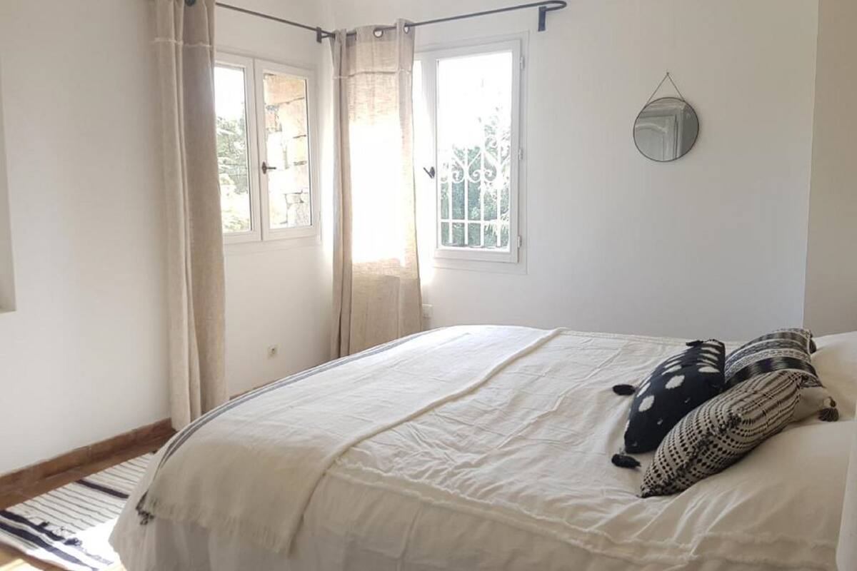 Un dormitorio con cama, cortinas, ventana y espejo adosado a la pared.