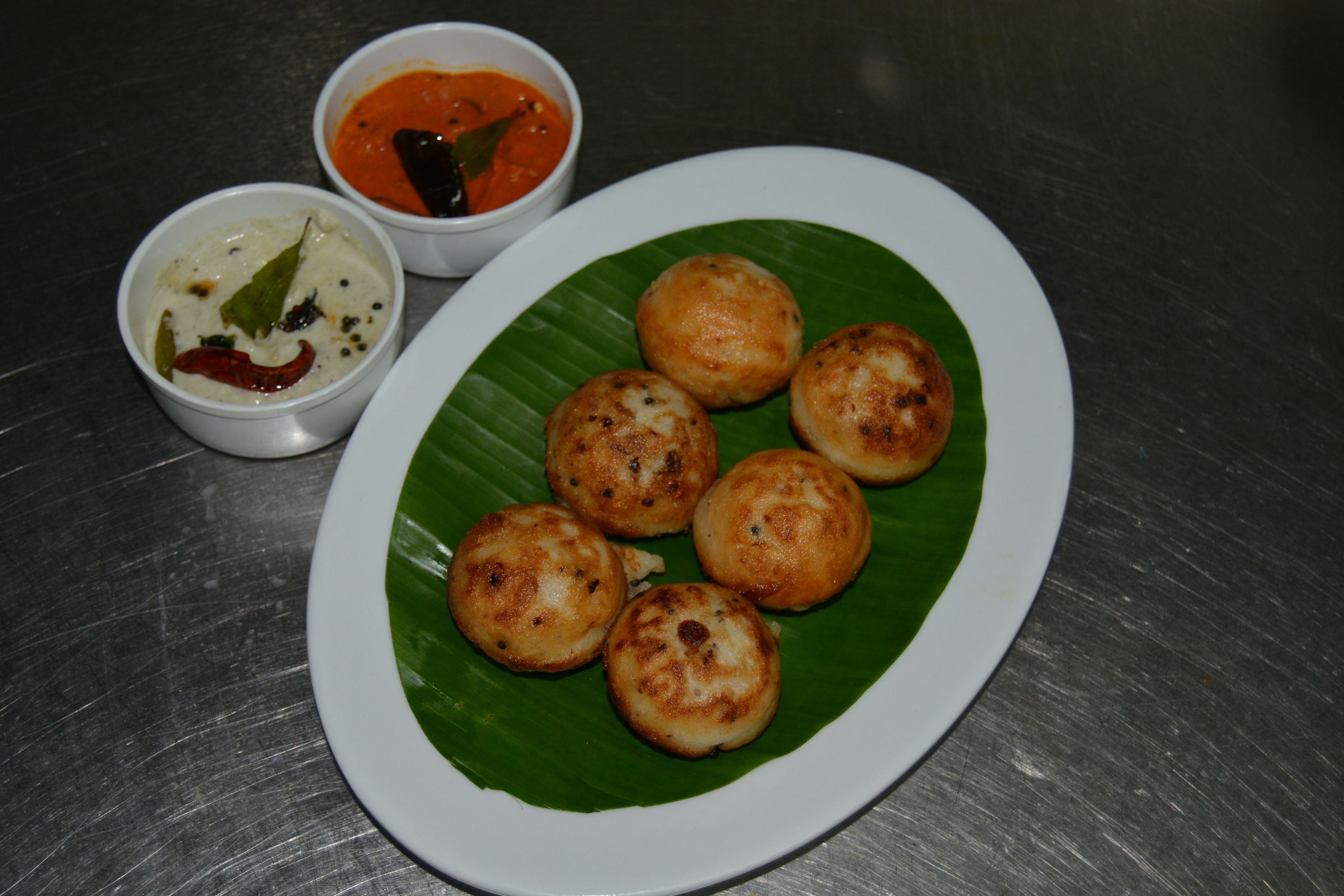 A plate of food with six round items on a banana leaf, accompanied by two small bowls of sauce.