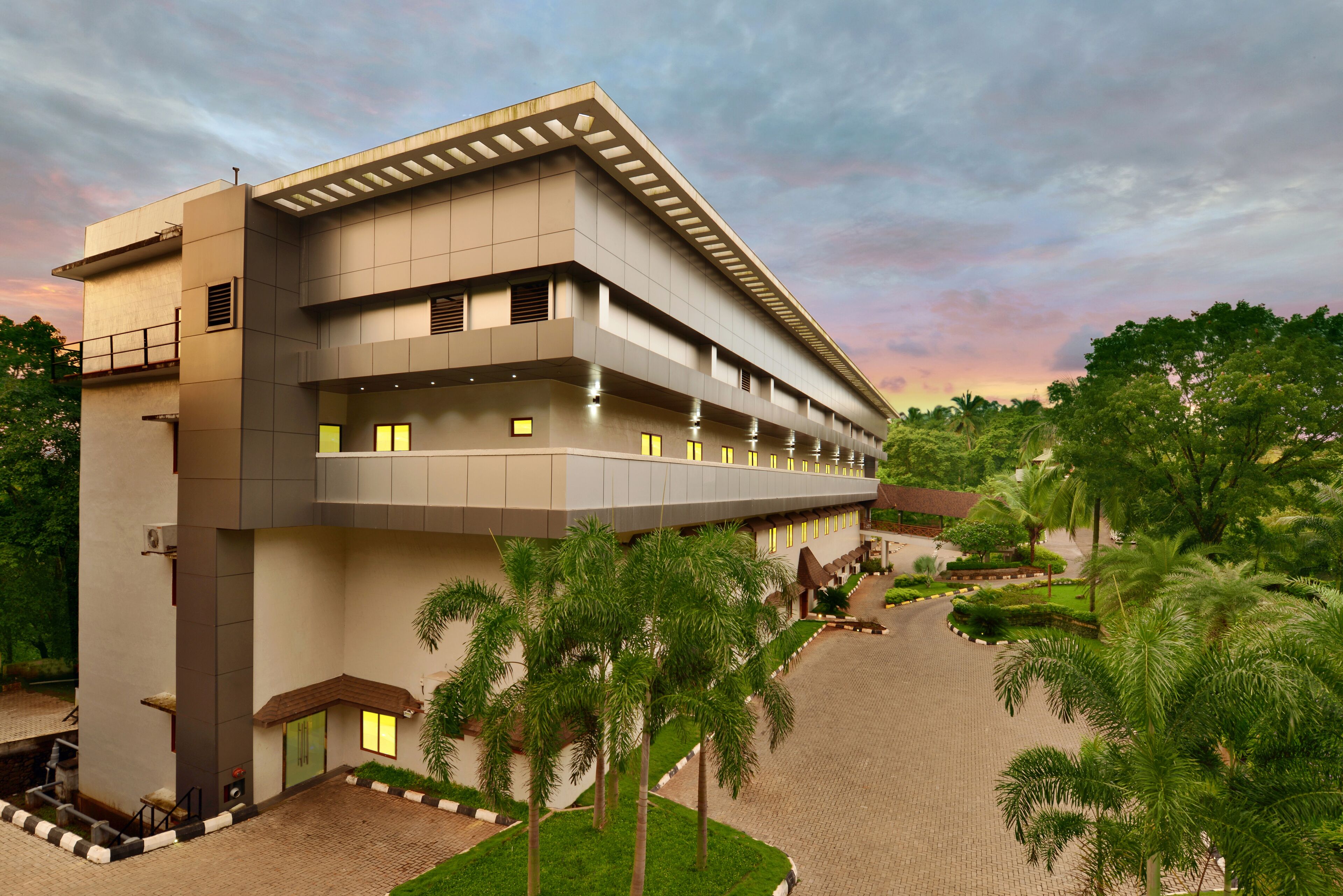 A modern hotel with a multi-story structure, a covered outdoor area, and a landscaped garden with palm trees.