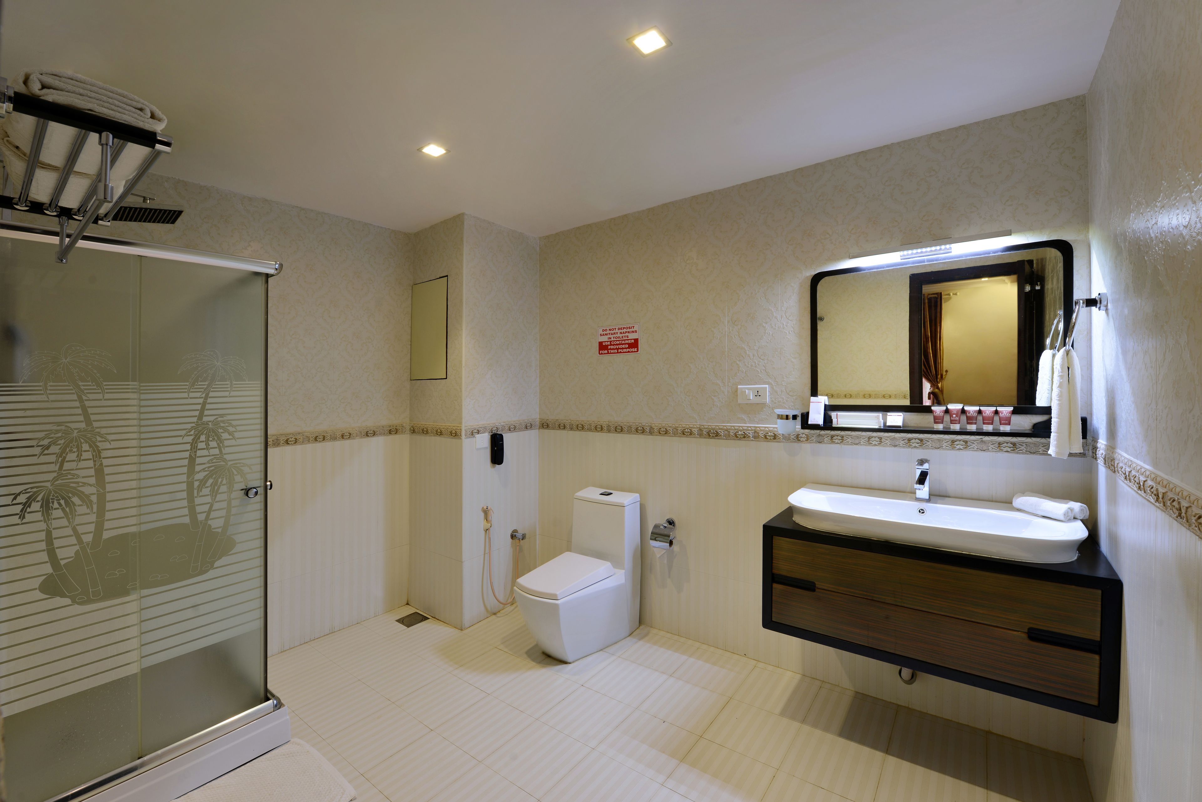 A bathroom with a glass-enclosed shower, a toilet, a sink with a mirror above it, and a towel rack.