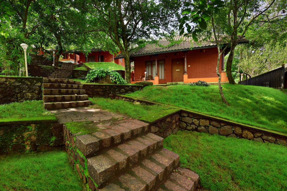 A traditional building with a red exterior, stone steps leading up to a wooden door, surrounded by lush greenery and a stone wall.